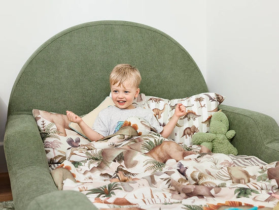 Child sitting on a green chair with a dinosaur-patterned blanket
